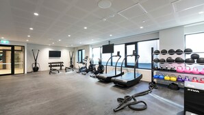 Une salle de sport moderne équipée de tapis de course, de vélos elliptiques et de poids libres.