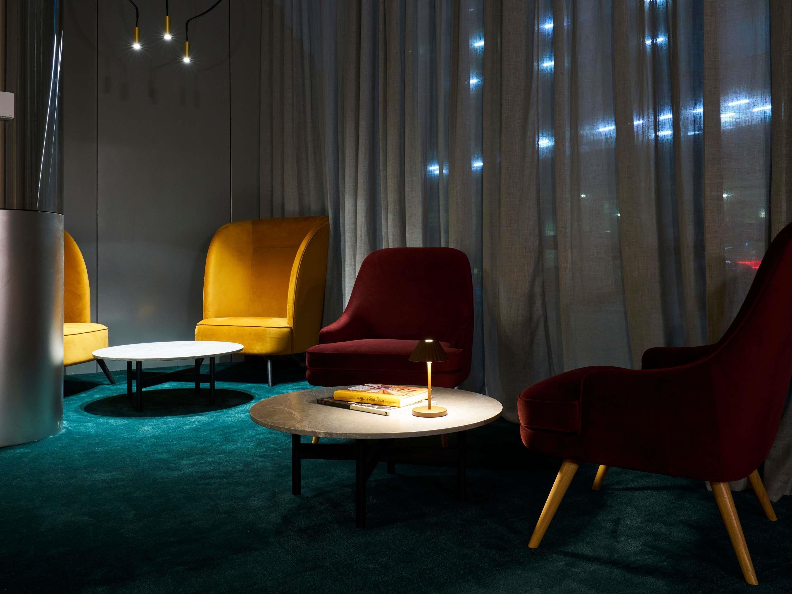 A room with a round table, two armchairs, a lamp, and a large window with curtains.