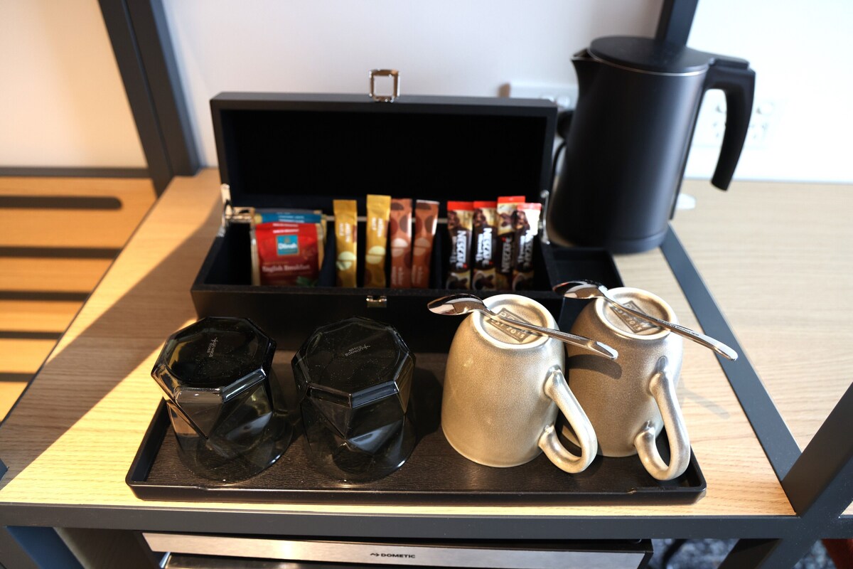 Un plateau contenant une machine à café, une tasse, un thermos et plusieurs dosettes de café, le tout posé sur une table.