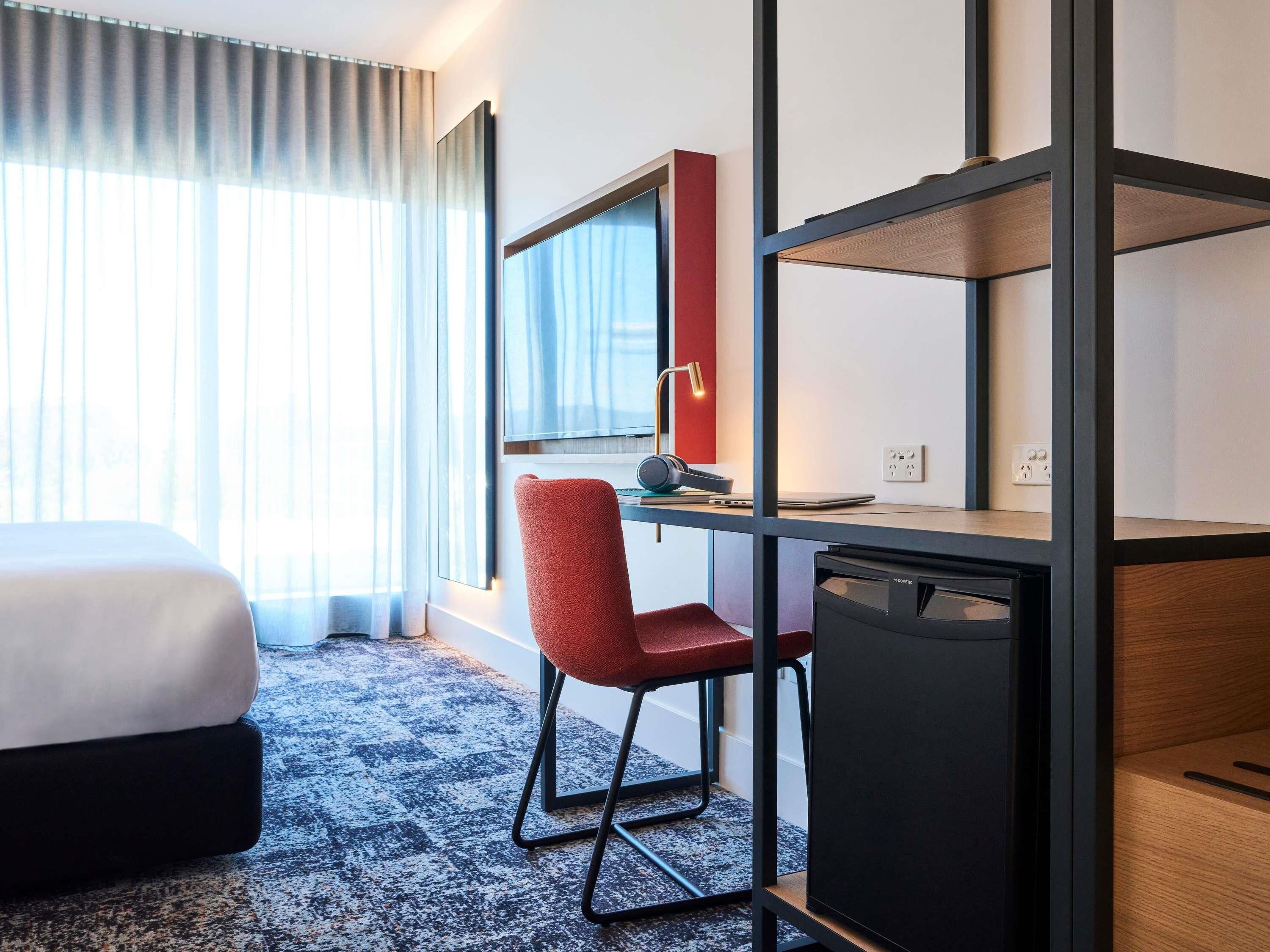 A hotel room with a bed, a desk with a chair, a lamp, and a small cabinet.