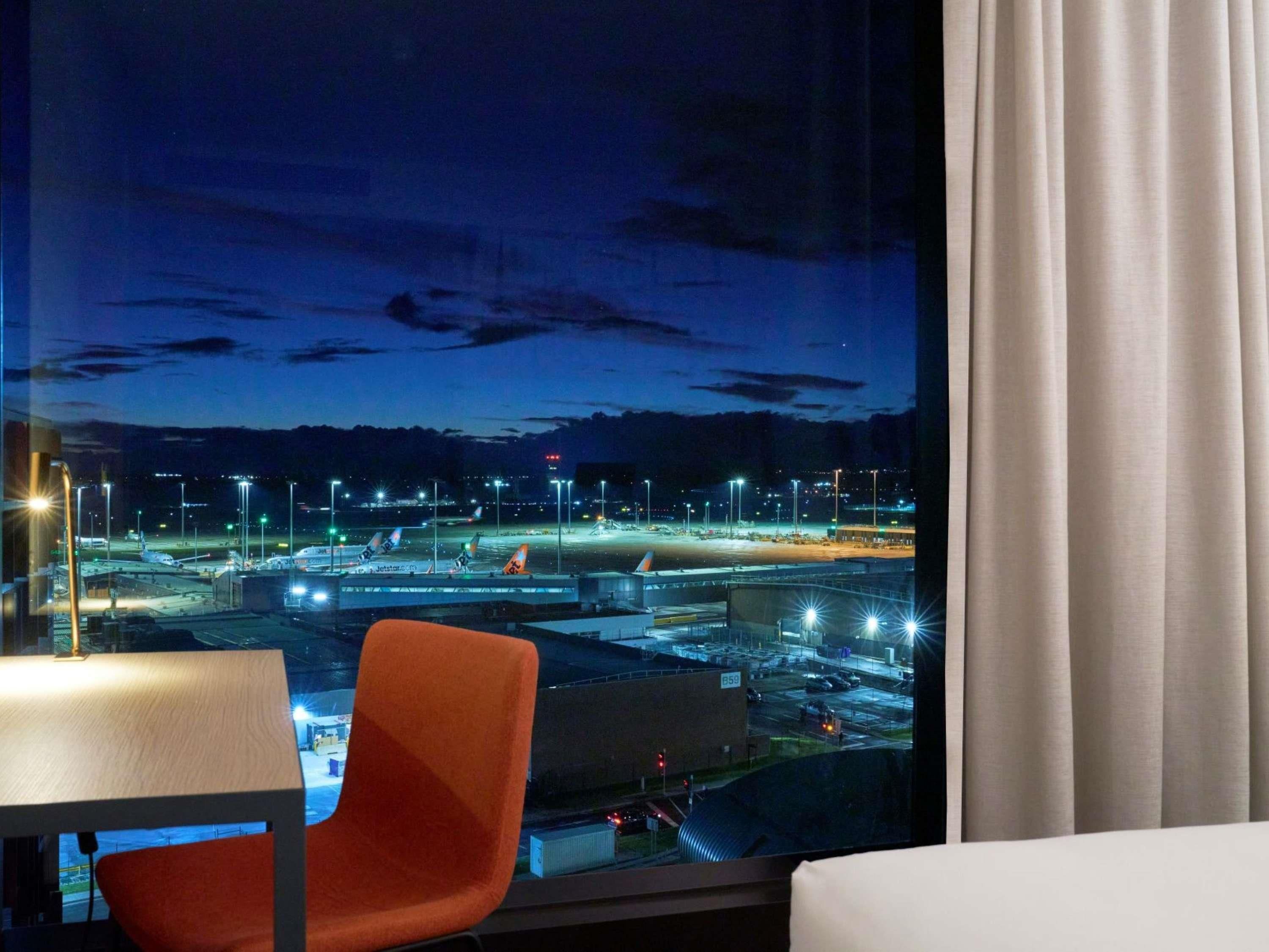 A hotel room with a large window overlooking an airport at night.