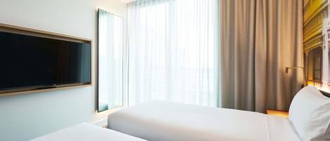 Habitación de hotel con una cama grande, un televisor de pantalla plana montado en la pared y una ventana con cortinas traslúcidas.