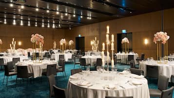 A banquet hall with round tables, white tablecloths, and tall floral centerpieces.