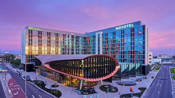 Ein modernes Hotel mit einer gebogenen Glasfassade, einem gut sichtbaren 'Novotel'-Schild und einem 'ibis Styles'-Schild.