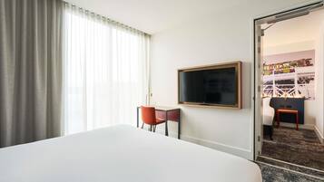 Une chambre d’hôtel avec un grand lit, un bureau avec une chaise, un téléviseur fixé au mur et une porte donnant sur une autre pièce.