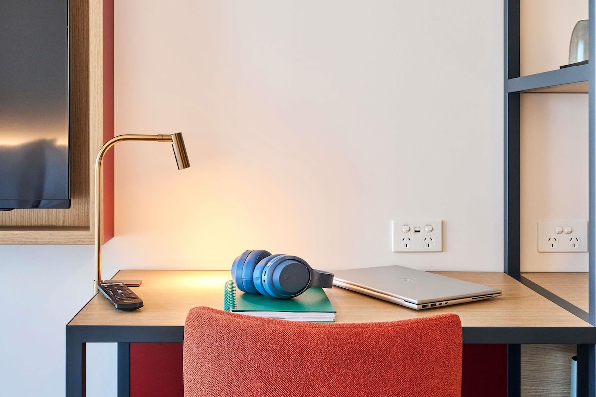 Un espace de travail comprenant un bureau, un ordinateur portable, un casque audio, un carnet, une télécommande et une lampe.