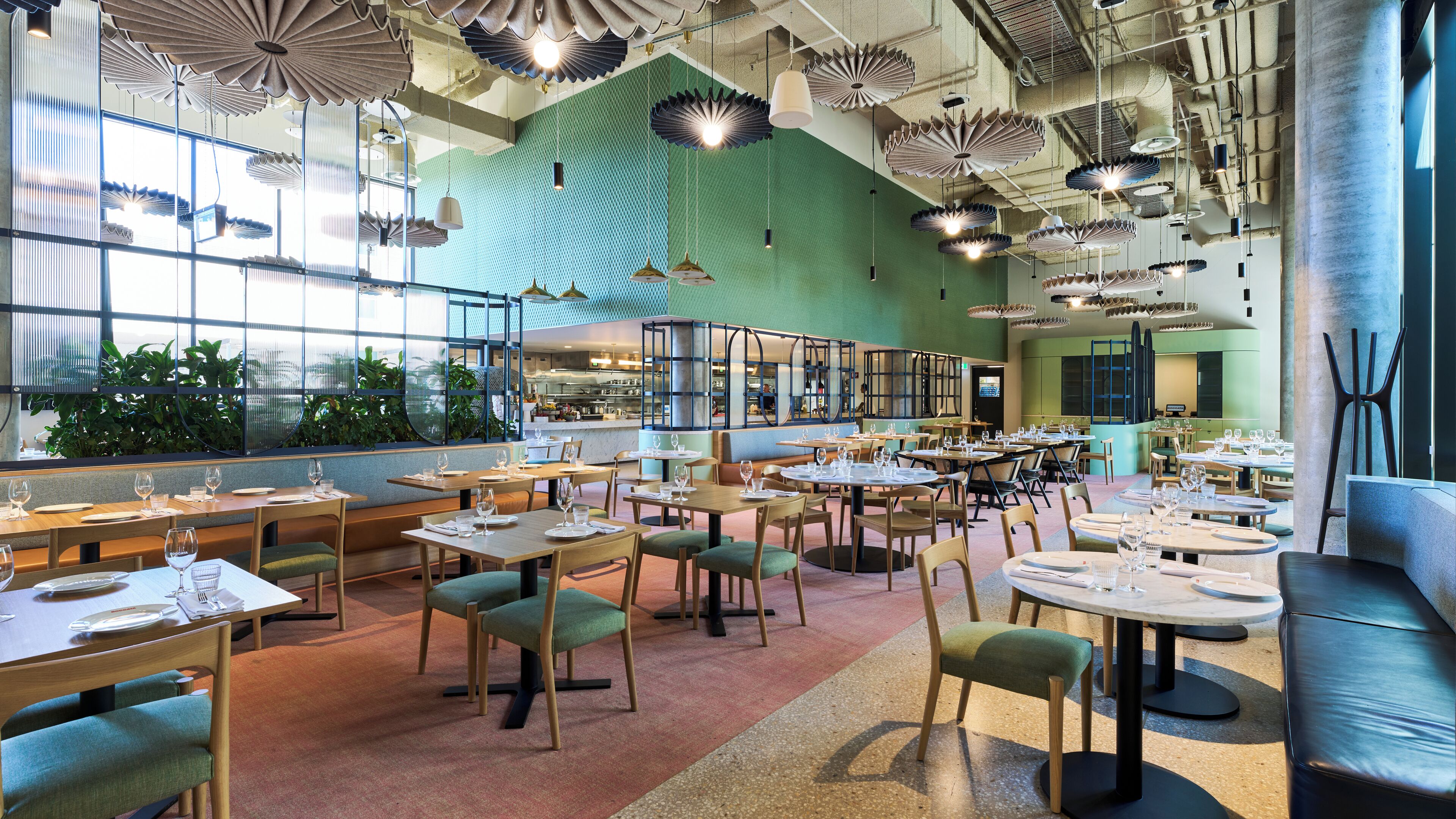 Un restaurant spacieux avec de hauts plafonds, des lampes en papier suspendues et différents types de sièges, notamment des tables et des banquettes.