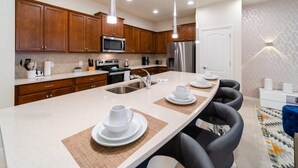 A modern kitchen with wooden cabinets, stainless steel appliances, and a central island with seating. - Premium 5-Bed Townhome, Themed, Perfect Location (Kissimmee)