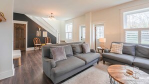 Una sala de estar con un sofá gris, una mesa de centro de madera y una escalera que lleva al piso superior.