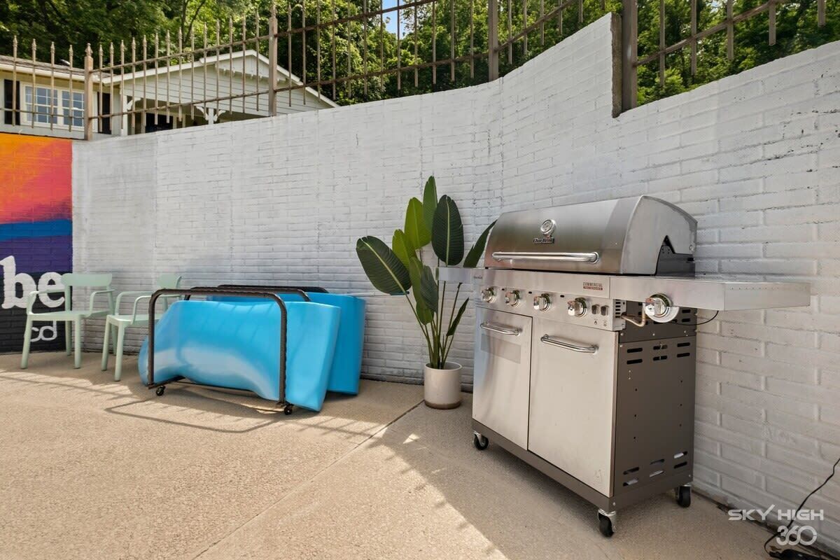 Ein tragbarer Grill, ein blauer Koffer und ein Blumentopf vor einer weißen Ziegelwand.
