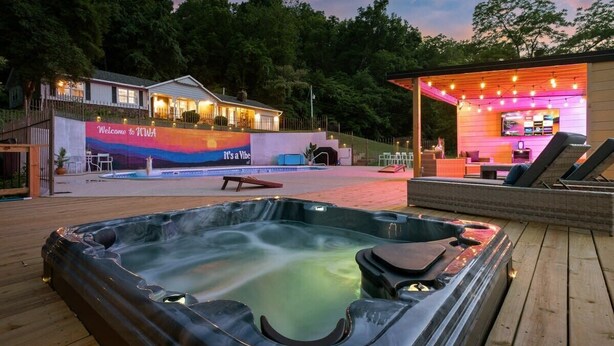 A hot tub on a wooden deck, a pool, and a building with a 'Welcome to WWA' sign. - Creekside Oasis w/ Pool & Hot Tub near Beaver Lake (Rogers)
