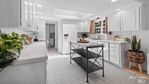 A modern kitchen with white cabinetry, a central island, and a dining area. - Creekside Oasis w/ Pool & Hot Tub near Beaver Lake (Rogers)