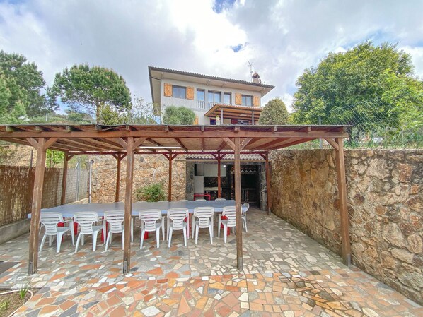 Un espacio de estar techado al aire libre con suelo de mosaicos y sillas de plástico blanco.