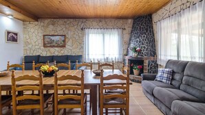 A cozy living room with a stone wall, a fireplace, a dining table with chairs, and a grey sofa.