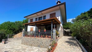 A two-story house with a stone facade, a balcony with potted plants, and a tiled patio.