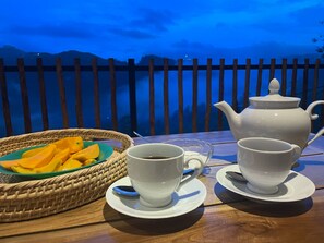 Une table avec une théière, deux tasses, un verre et un panier de fruits.