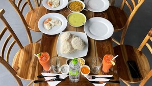 A wooden dining table set with plates of food, bowls, cups, and glasses of beverages.