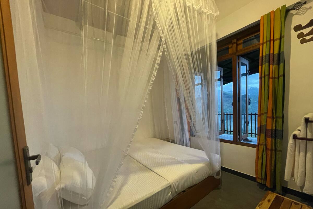 A room with a bed under a canopy, a window with curtains, and a wooden bench.