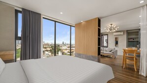 A modern hotel room with a large bed, a dining area, and a view of the cityscape. - Rose Sea Hotel & Apartment (Da Nang)