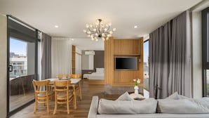 A modern living room with a sofa, dining table, and chairs. There is a TV mounted on the wall and a chandelier. - Rose Sea Hotel & Apartment (Da Nang)