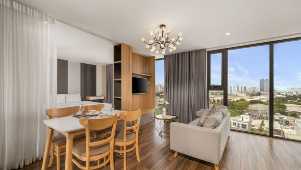 A modern living room with a dining area, large windows with a city view, and a chandelier. - Rose Sea Hotel & Apartment (Da Nang)