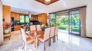 Una cocina moderna con armarios de madera, un comedor con una mesa grande y sillas, y vistas a la vegetación a través de puertas correderas amplias.