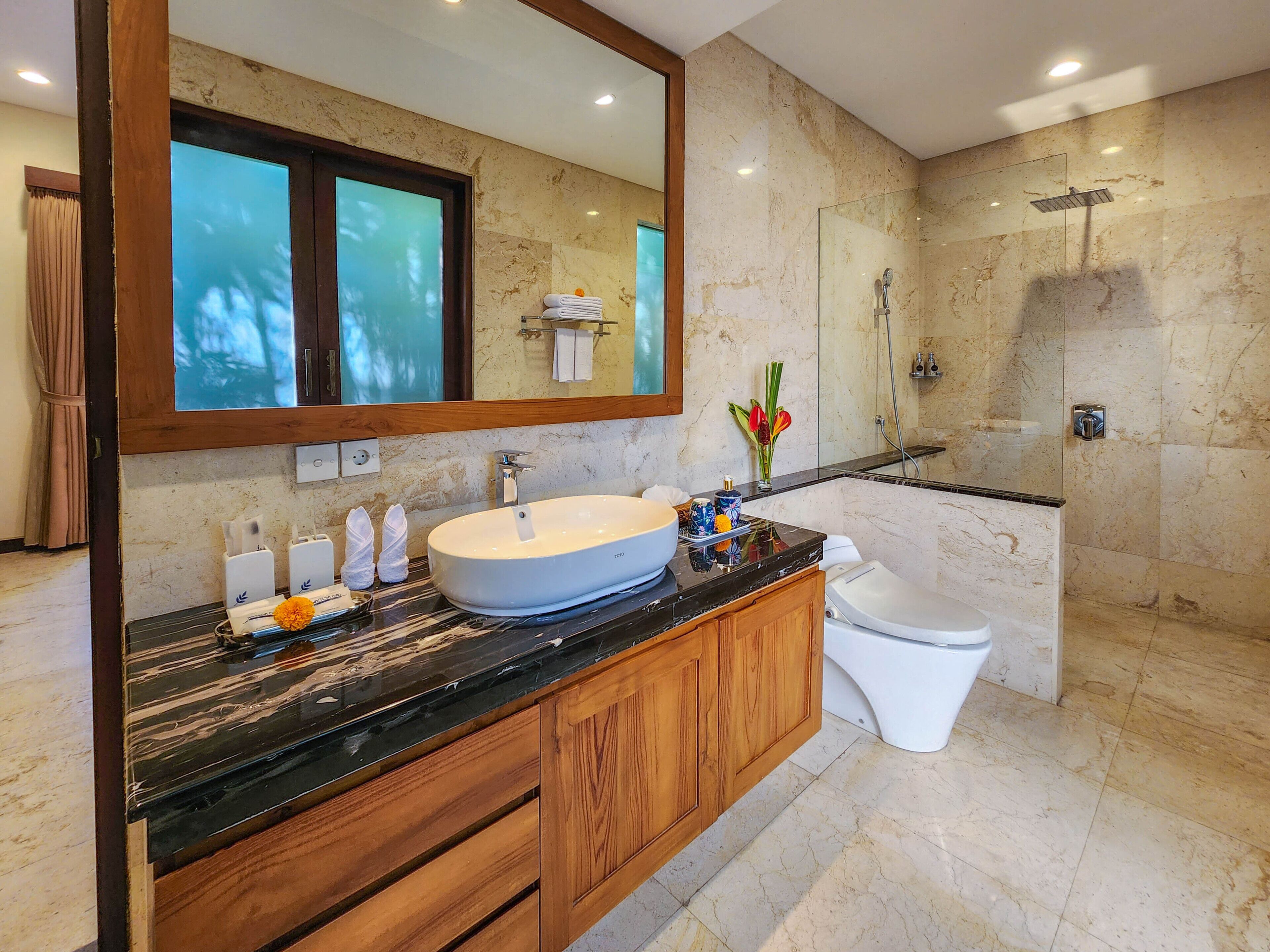 Une salle de bain moderne avec un grand lavabo ovale, un meuble-lavabo en bois, des toilettes, une cabine de douche en verre et un grand miroir.