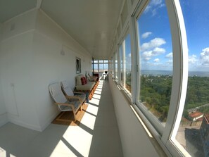 Un balcone con una fila di sedie e un tavolo, ampie finestre che offrono vista sulla città e sul verde.