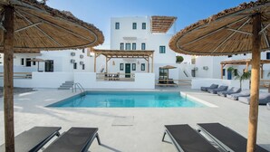 A pool area with lounge chairs, a wooden pergola, and a white building in the background.