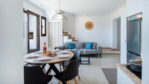 A modern kitchen with a built-in oven, a dining area with a round table and chairs, and a grey sofa with blue cushions in the background.