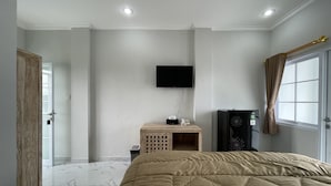 A bedroom with a bed, a television mounted on the wall, a small wooden side table, and a window with curtains. - Casa Rani Canggu (Munggu)