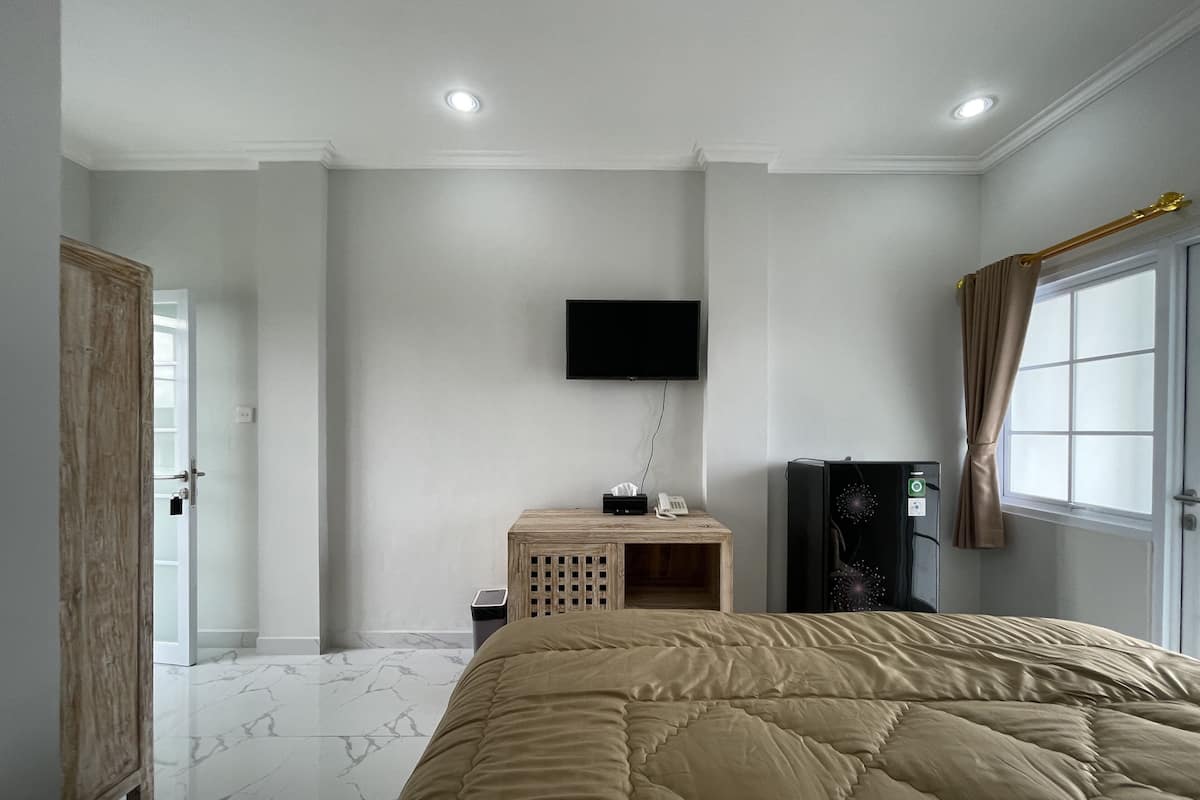 Ein Schlafzimmer mit einem Bett, einem an der Wand befestigten Fernseher, einem kleinen Nachttisch und einem Fenster mit Vorhängen.
