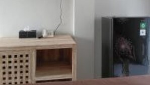 A room with a mounted television on the wall, a wooden cabinet with a small table, and a refrigerator. - Casa Rani Canggu (Munggu)