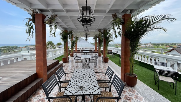 A covered outdoor patio with a patterned floor, tables, chairs, and potted plants. - Casa Rani Canggu (Munggu)