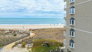 Un hotel frente a la playa con arena, vistas despejadas del océano y un jardín cercado.