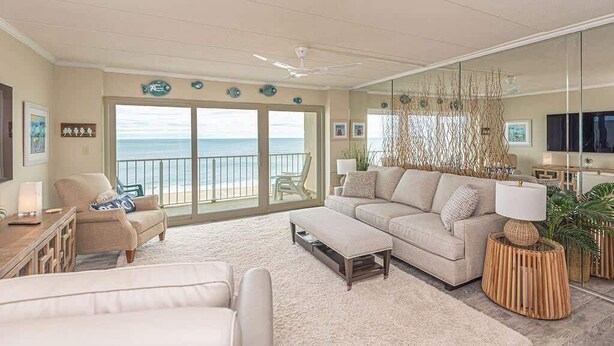 Un salón amplio con un gran ventanal con vista al océano, un sofá cómodo, una mesa de centro y un televisor.
