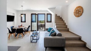 A modern interior with a dining area, sofa, staircase, and a wall-mounted decorative piece.