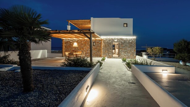A modern house with a stone exterior, a wooden pergola, and a patio with outdoor furniture.