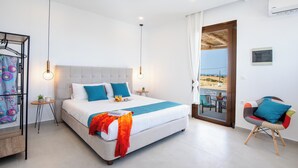 A modern hotel room with a large bed, a small table with a plant, and a view of the outdoors through a glass door.