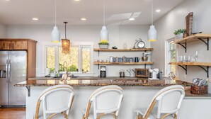 Une cuisine moderne dotée d’un îlot central, de tabourets de bar, de luminaires suspendus et d’étagères intégrées.