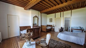 Quarto com vigas de madeira, uma cama, uma cadeira, cômoda e espelho.