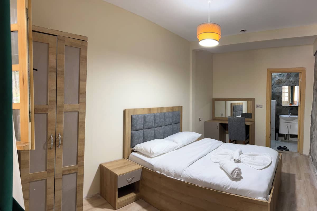 A bedroom with a wooden bed, a nightstand, a wardrobe, and a bathroom visible through an open door.