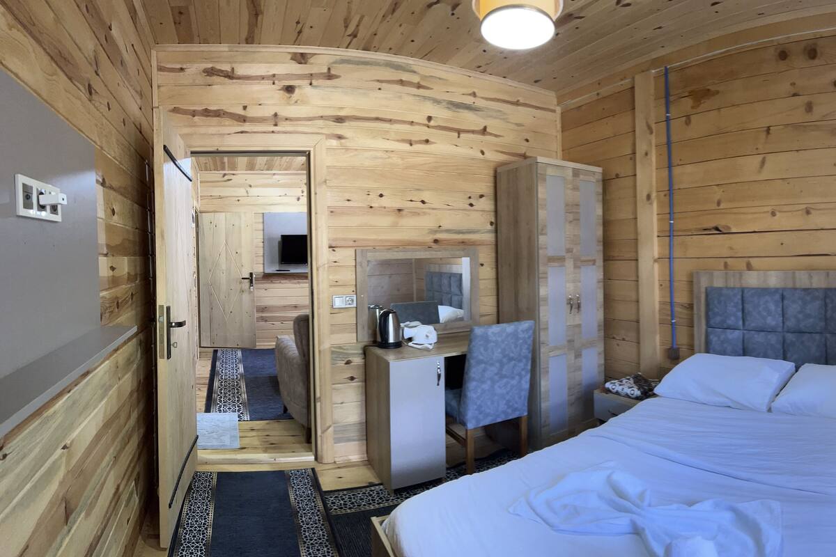 A wooden cabin room with a bed, a desk, a chair, and a wardrobe.