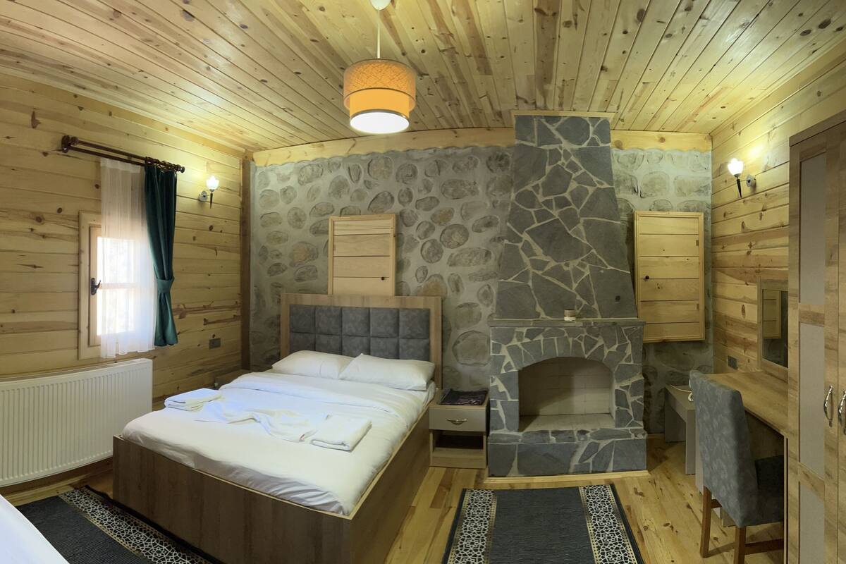 A wooden cabin bedroom with a stone fireplace, a bed, a bedside table, and a TV mounted on the wall.