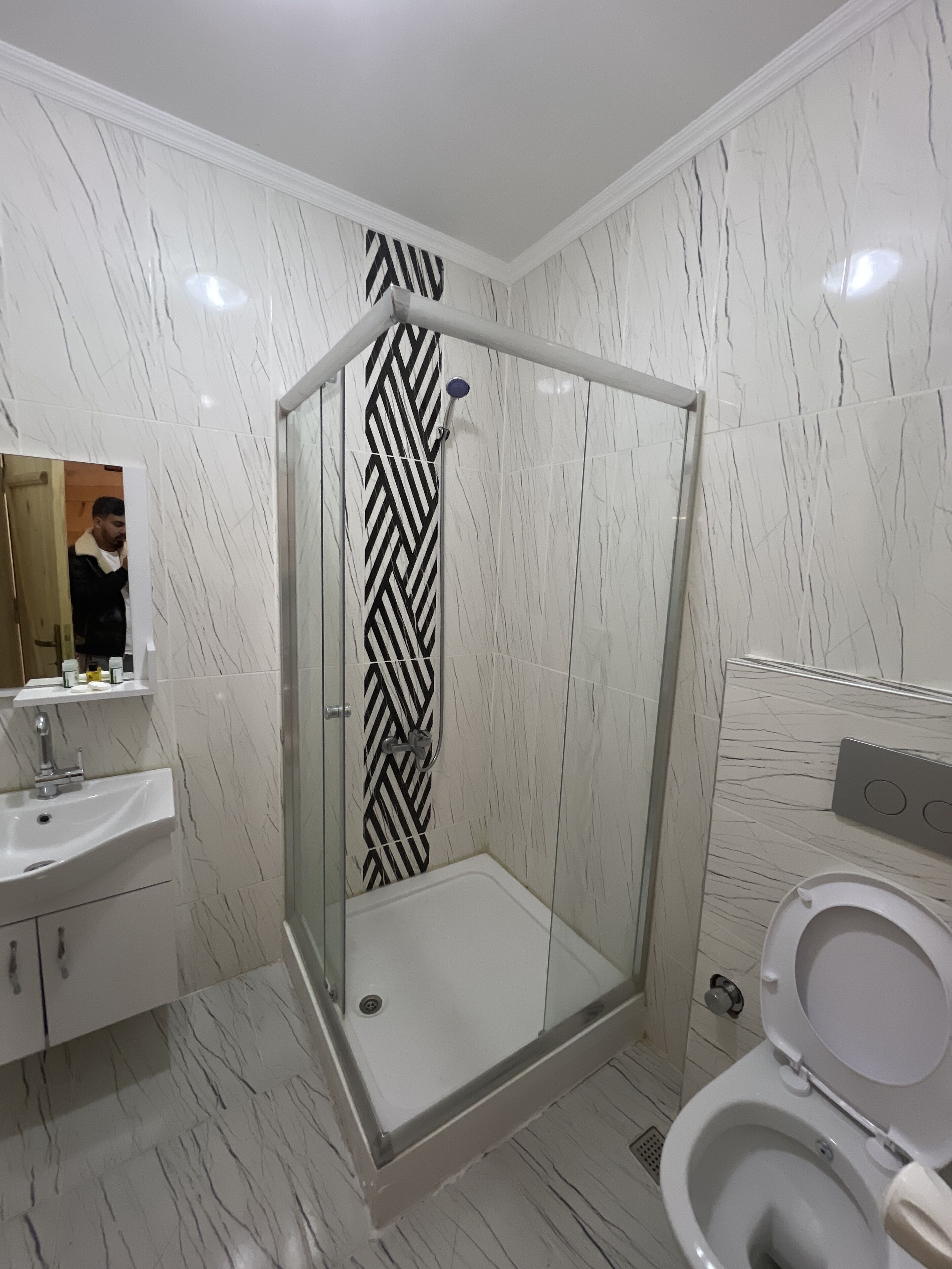 Een moderne badkamer met een douchecabine van glas, een witte wastafel en een toilet.