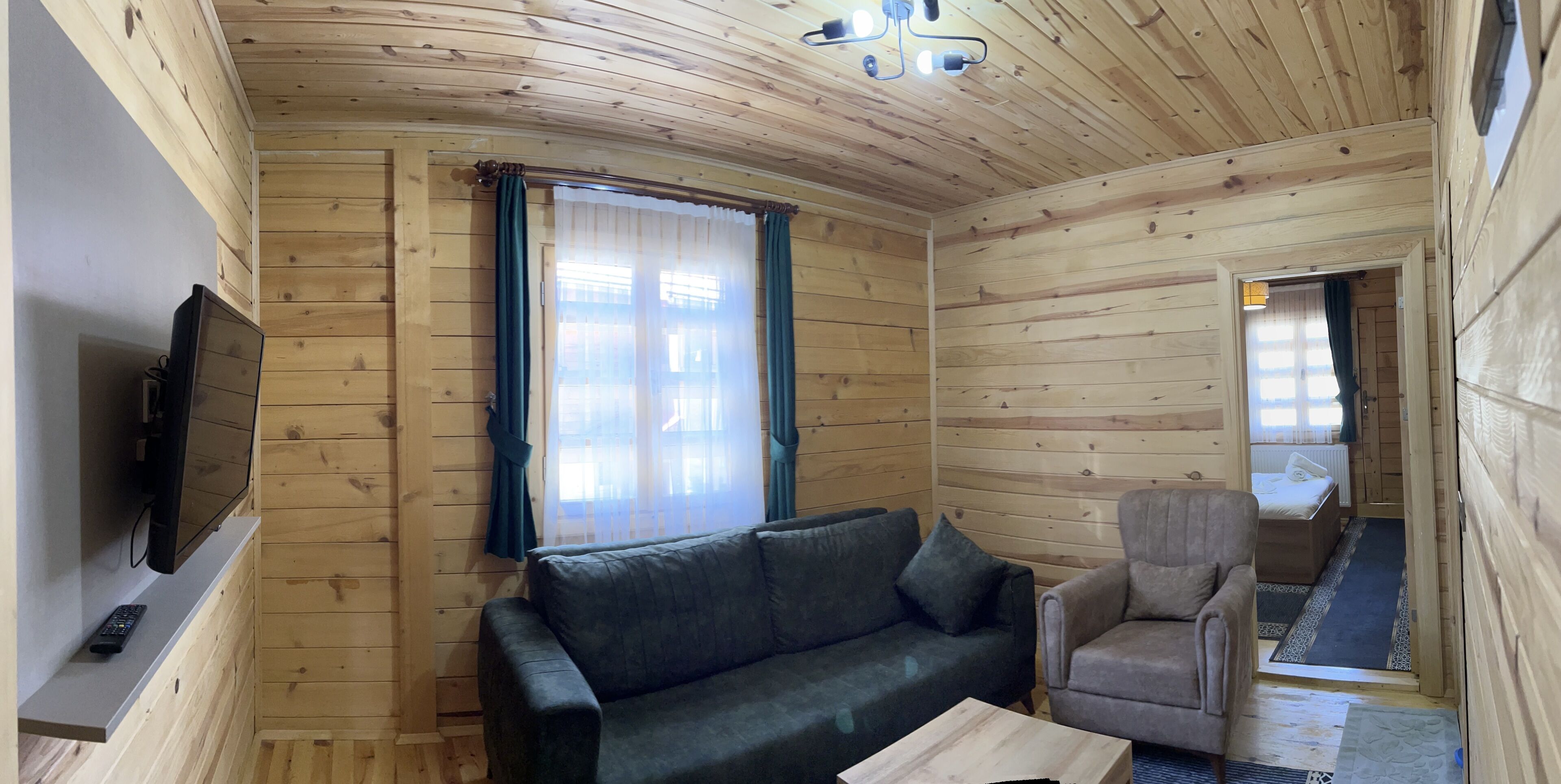 L’intérieur d’un chalet en bois, avec un canapé, un fauteuil et un téléviseur posé sur une étagère.