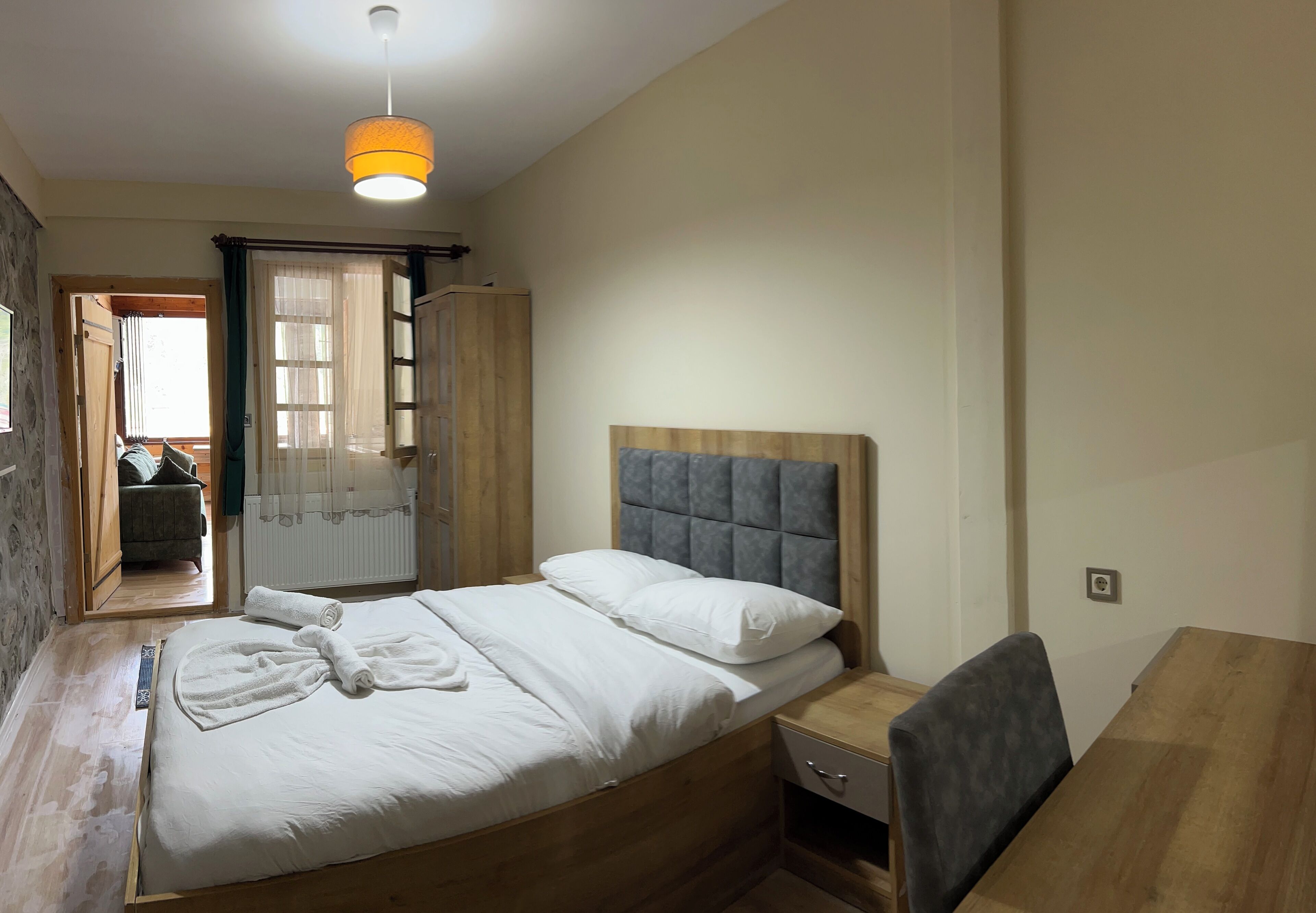 A bedroom with a wooden bed, a bedside table, a chair, and a window with curtains.