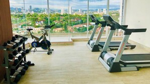 Un gimnasio con cintas de correr y una bicicleta estática, amplias ventanas con vistas a la ciudad.