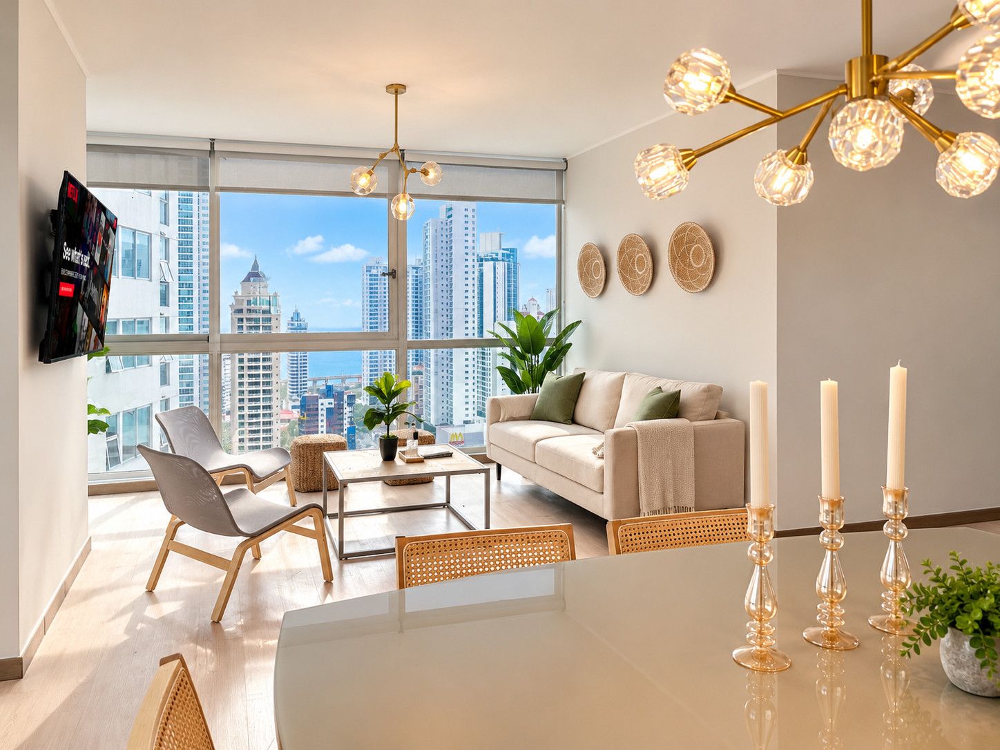 A modern living room with a city view, a sofa, a coffee table, and a dining table with candles.