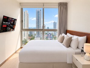 A hotel room with a large window, a bed with white bedding, a wooden headboard, a nightstand with a lamp, and a water bottle.
